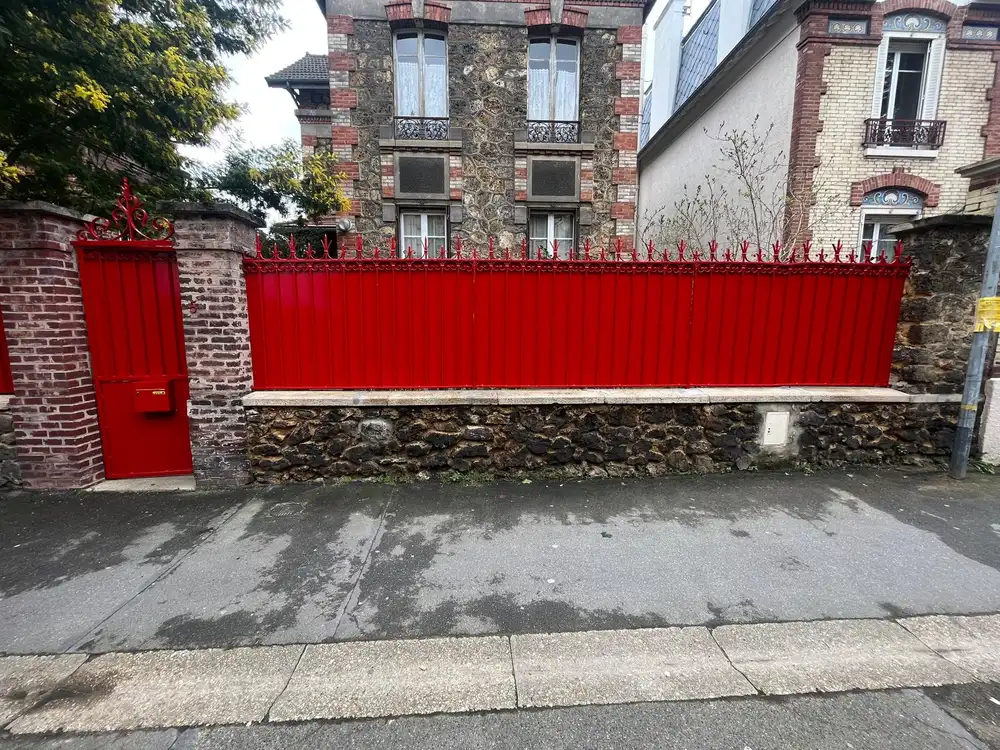 Clôture métallique repeinte en rouge et mur en pierre rénové
